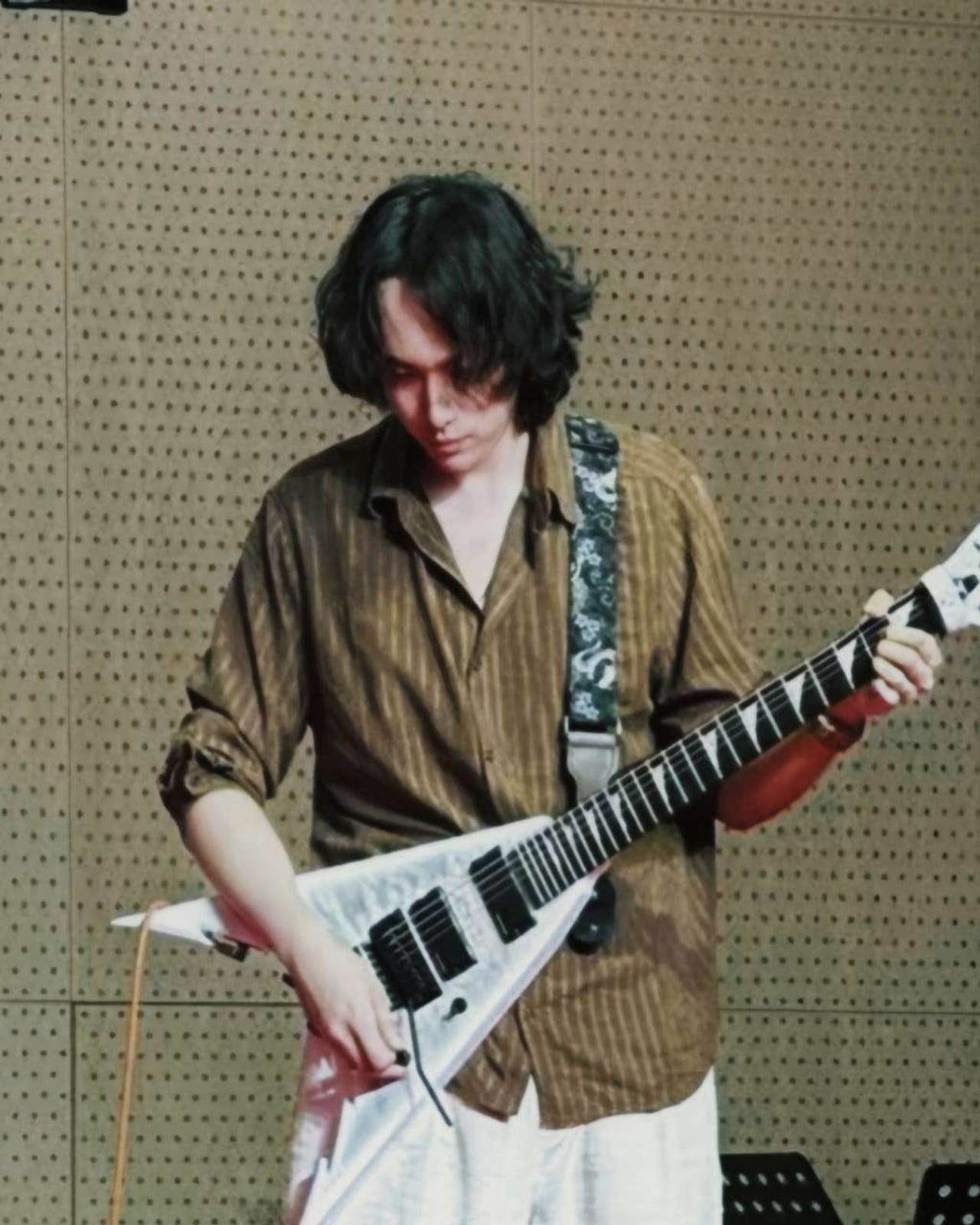 Shay Chen playing a white electric guitar in a rehearsal room.