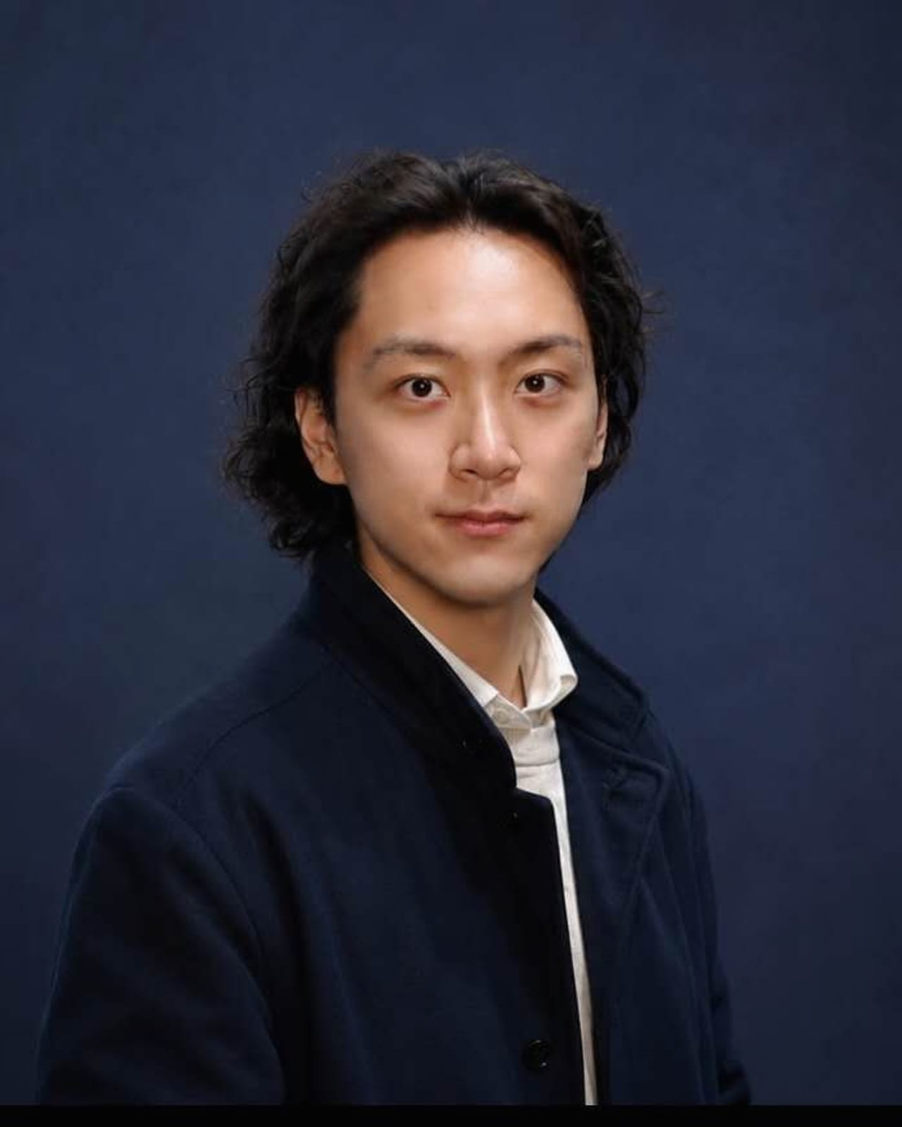 Shay Chen in a navy jacket against a deep blue studio background.